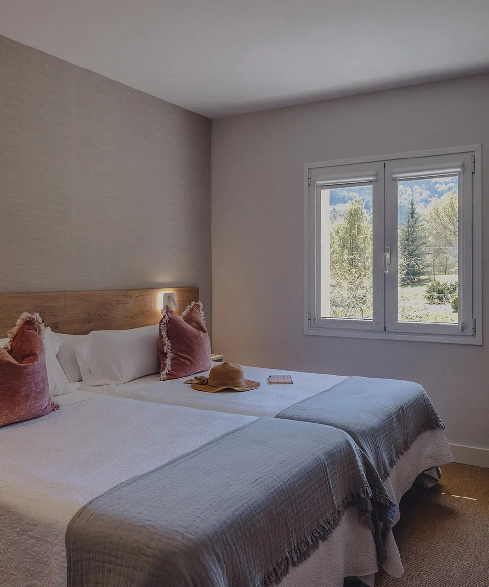 A twin-bedded room at Amalurra with two single beds, soft natural light, and a window onto the Basque mountain valley.