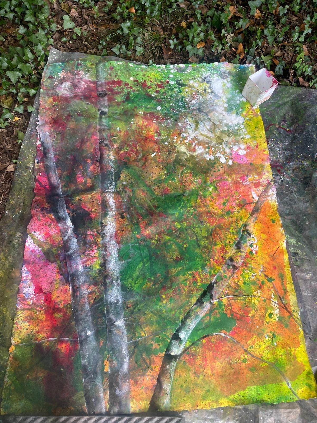 A vibrant abstract painting on plastic sheeting laid out in the forest.