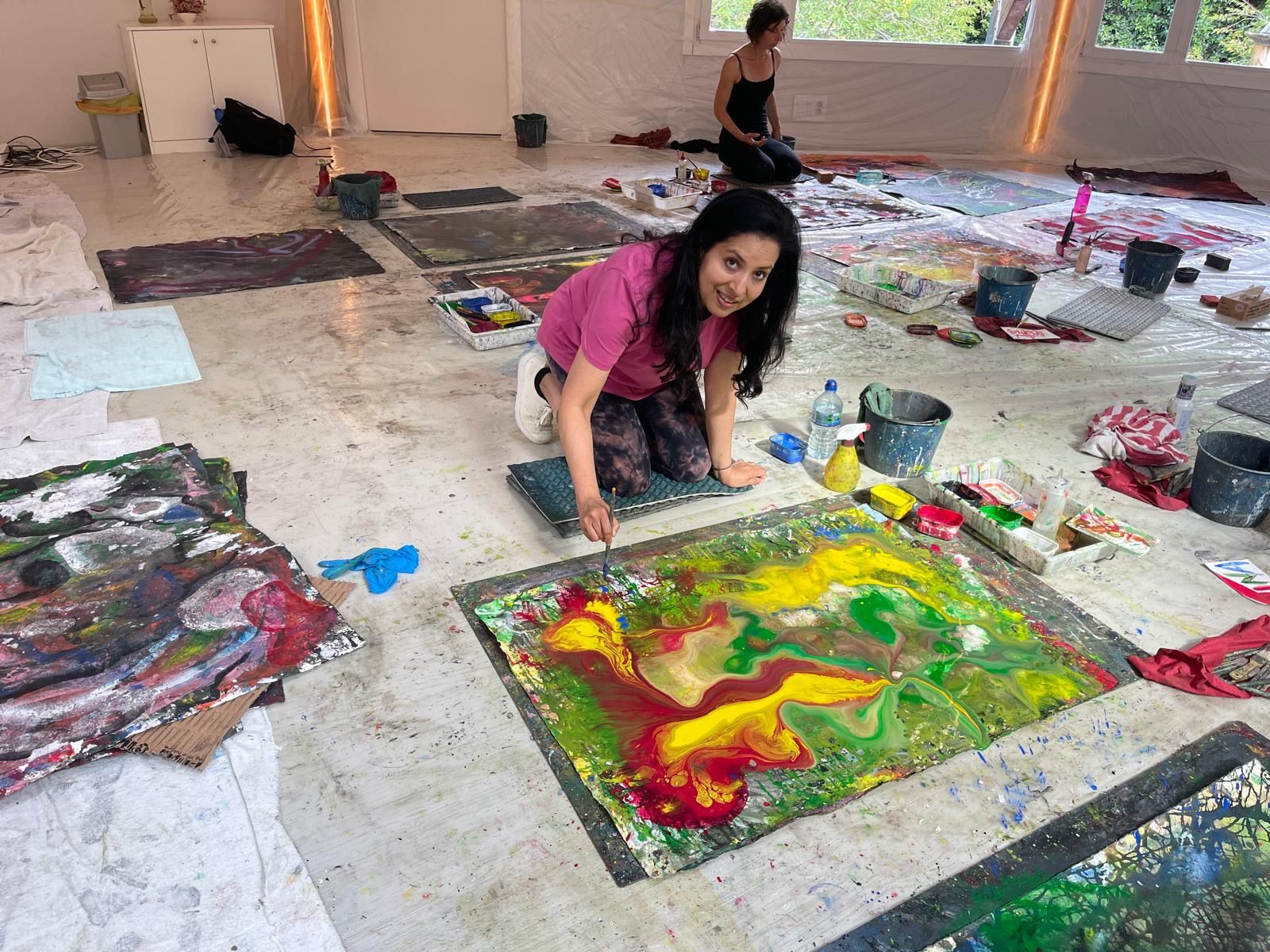 A workshop participant working on a large canvas indoors — paints and brushes in foreground.