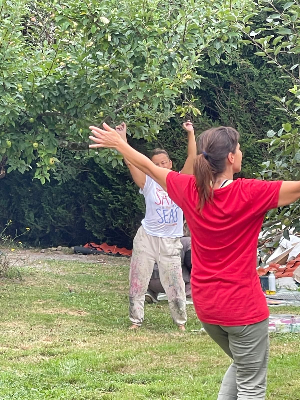 Two participants in an apple orchard with arms outstretched, mid-movement.