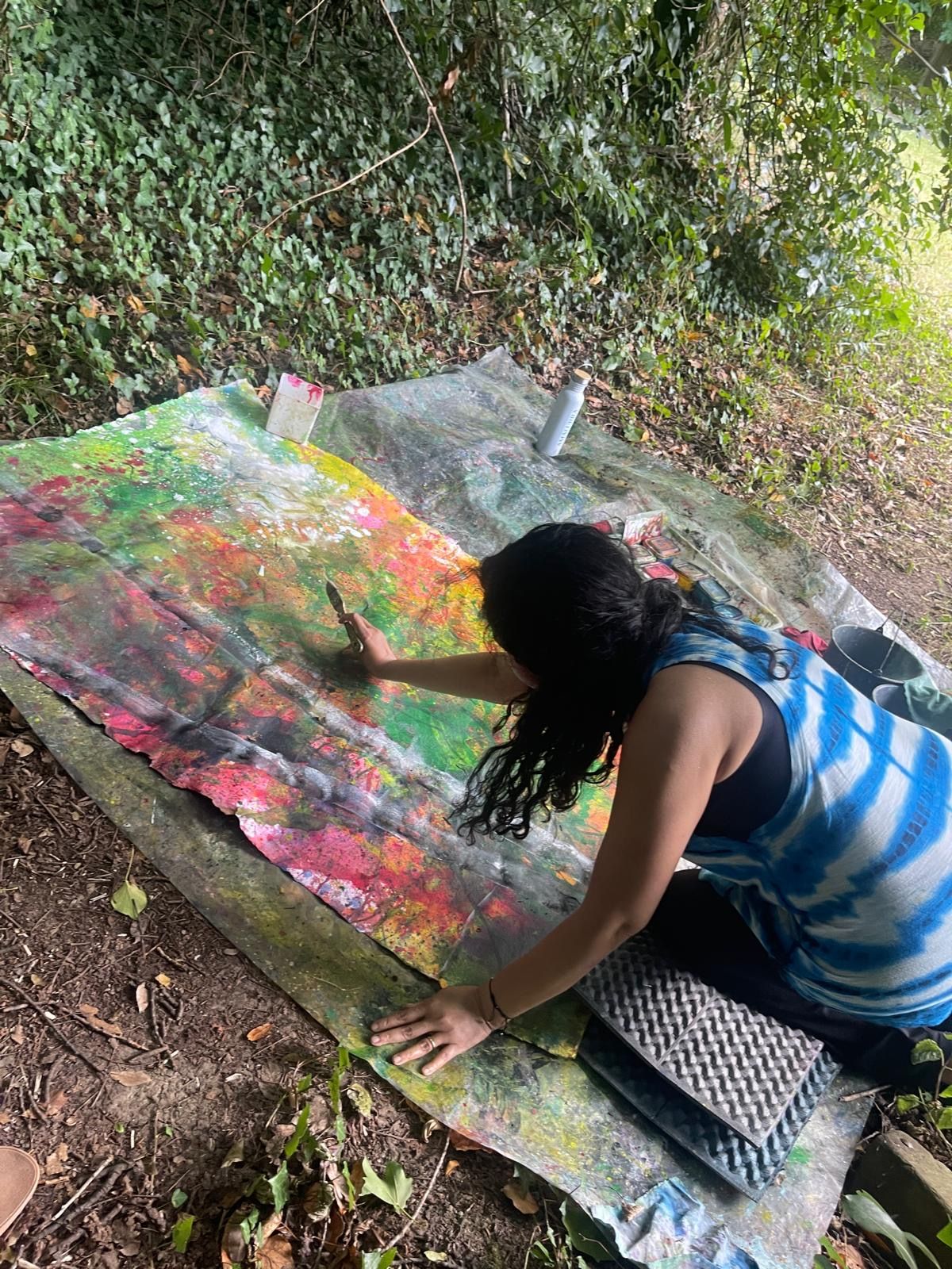 A painter working outdoors in the forest, brush in hand and palette beside her.