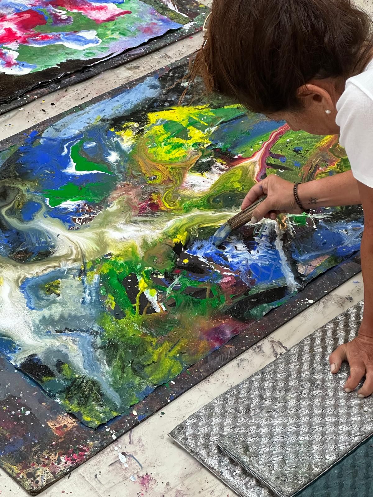 A close-up of a hand painting with a brush — vibrant blues and greens on a canvas in progress.