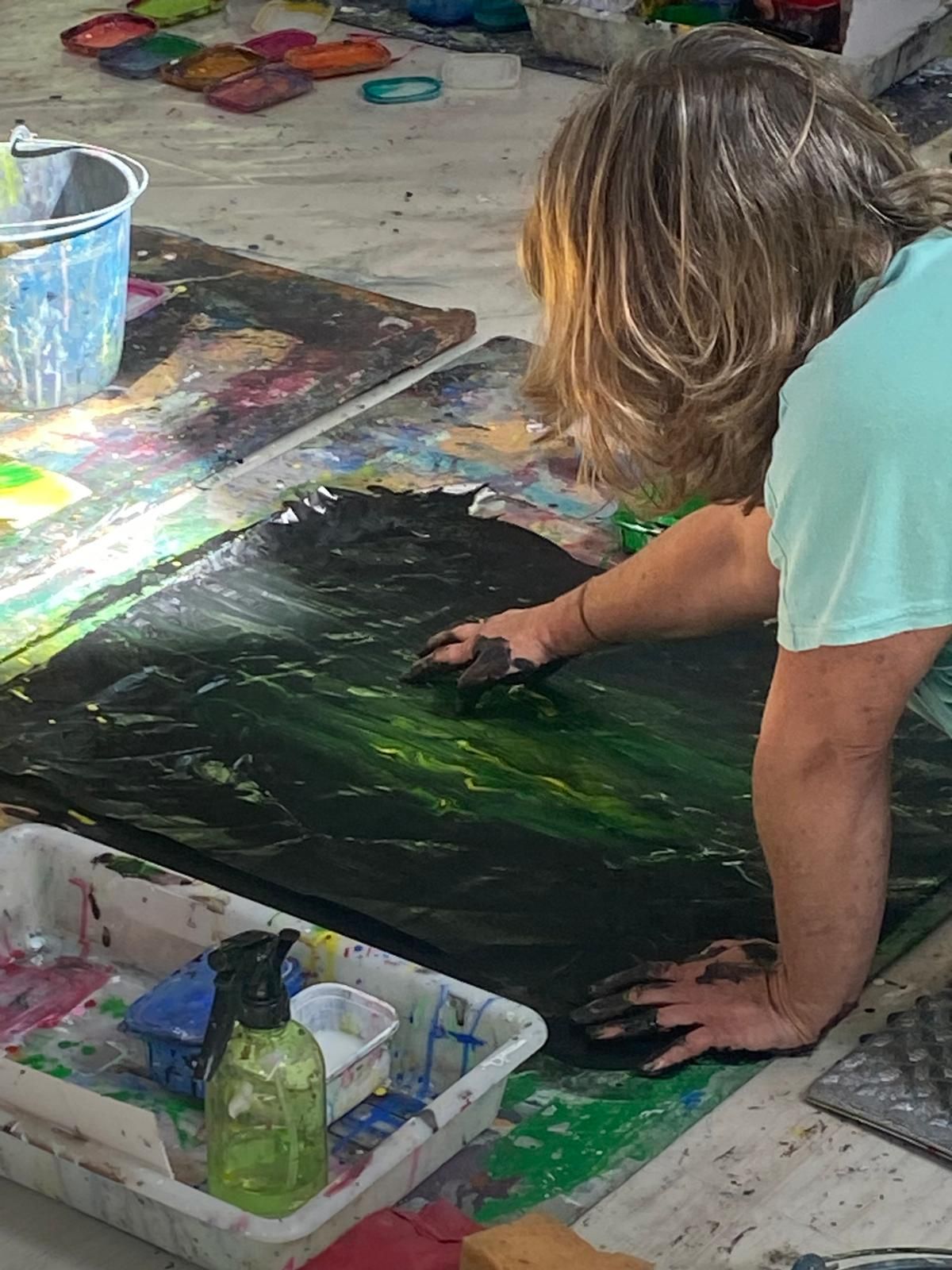 A close-up of bare hands working dark-green paint across a large canvas — Primal Painting in progress.